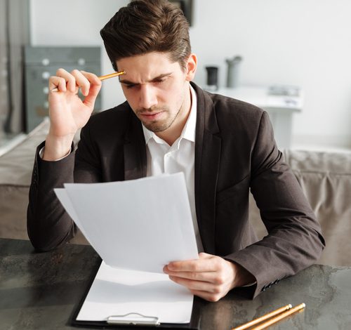 Concentrated young businessman working indoors Photo of concentrated young businessman working indoors. Looking aside holding documents.